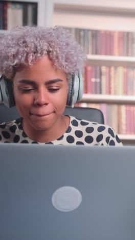 young african american woman listening to music on headphones works with laptop
