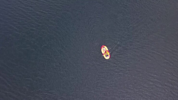 A lone inflatable boat floats gently on a vast lake. Ideal for themes of solitude or adventure. Captured from an aerial perspective.