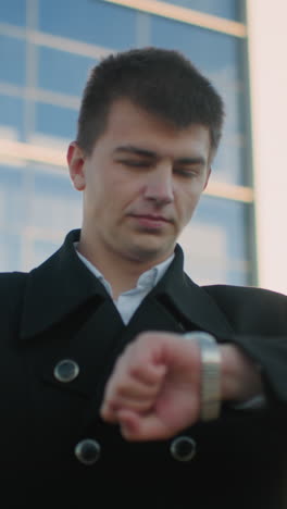 hombre con ropa negra revisa su reloj de muñeca con una sutil sonrisa mientras la luz del sol se refleja en su hombro, emanando confianza y precisión, el fondo presenta un edificio de vidrio moderno