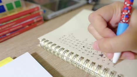 Close-up-shot-of-a-hand-writing-and-practicing-Japanese-letters-on-a-notebook-on-her-desk