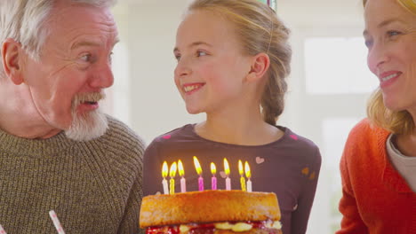 grandparents with granddaughter celebrating blowing out candles on birthday cake at home together