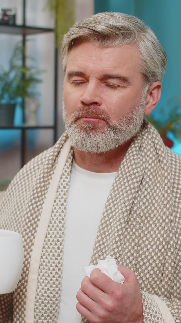 Mature man sitting at home holding napkin wipes snot drinking hot beverage or cold medicine at home