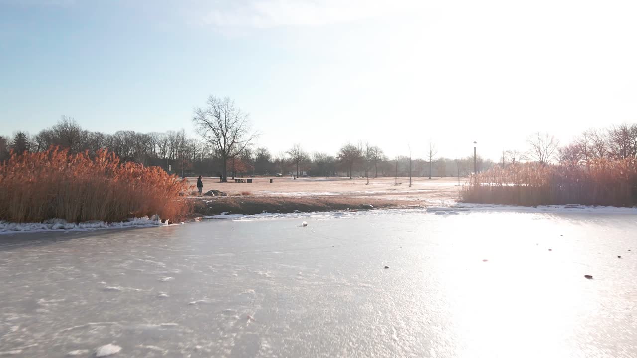 A dynamic aerial shot captures a frozen lake as the camera glides toward a man running along a path.