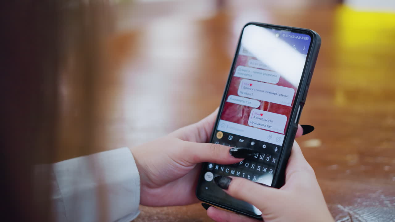 Rear view of lady chatting on phone with her ex, typing messages on smartphone placed on wooden table, with blurred background and bokeh light effects