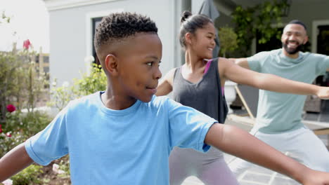 Happy-african-american-father,-son-and-daughter-practicing-yoga-standing-in-garden,-slow-motion