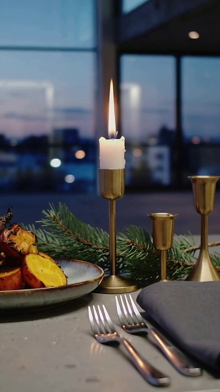 Vertical video: Tilting camera revealing brass candle flickering at home table with plate at dusk