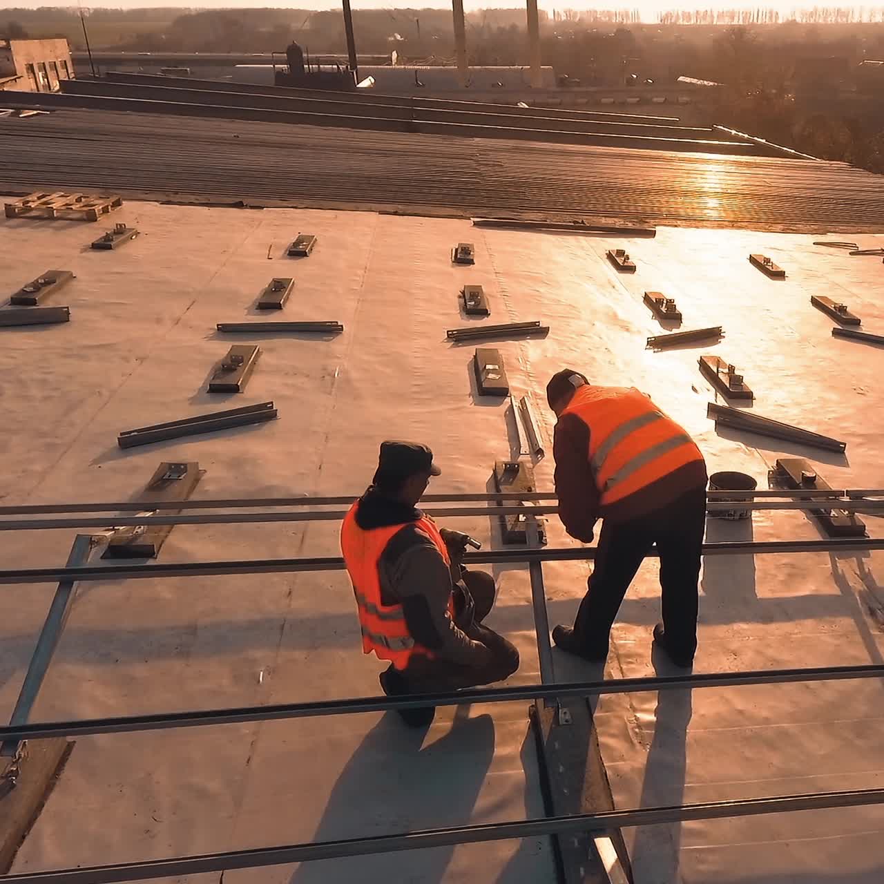 Two workers install metal basis on roof. Technicians in protective uniform prepare place for solar panels. Slow motion. Camera moves around.