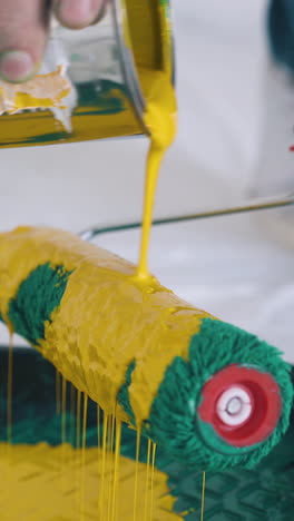 cu: professional builder pours bright yellow paint onto green roller above plastic tray on floor covered with foil closeup
