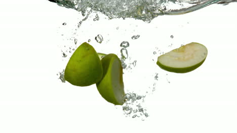 segmentos de manzana sumergiéndose en el agua sobre un fondo blanco