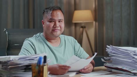 close up of fat asian man smiling to camera while working with documents at the office