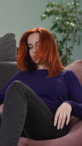 woman with ginger hair comes to sit in bean bag chair after long day of work in office. happy businesswoman enjoys relaxing in living room slow motion