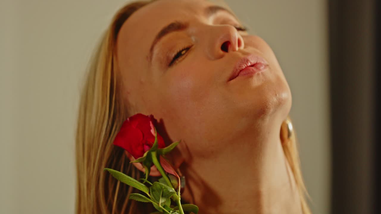 Close-up of a blonde woman sensually smelling a red rose