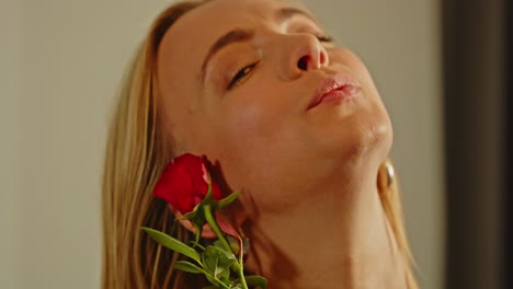 close-up of a blonde woman sensually smelling a red rose