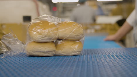 bread buns in a plastic bag on a conveyor being picked up by a worker