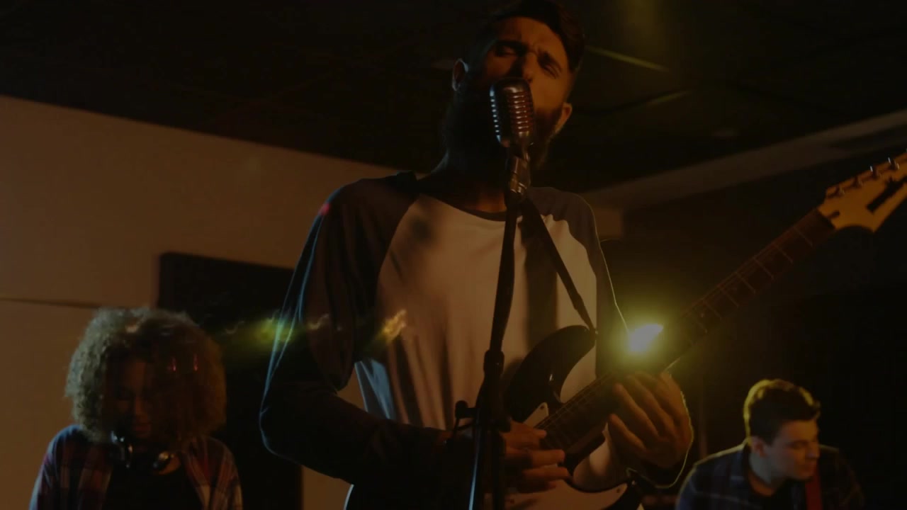 Cantante che si china sul microfono e canta, causando bagliori animati dell'obiettivo che si diffondono sulla performance della band.