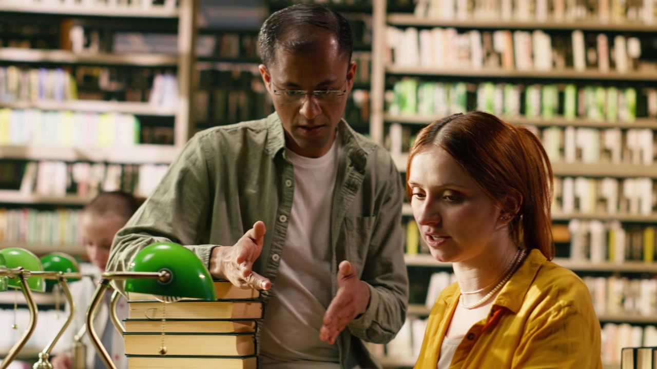 Tutor che guida una giovane donna che lavora al laptop a una scrivania della biblioteca universitaria.