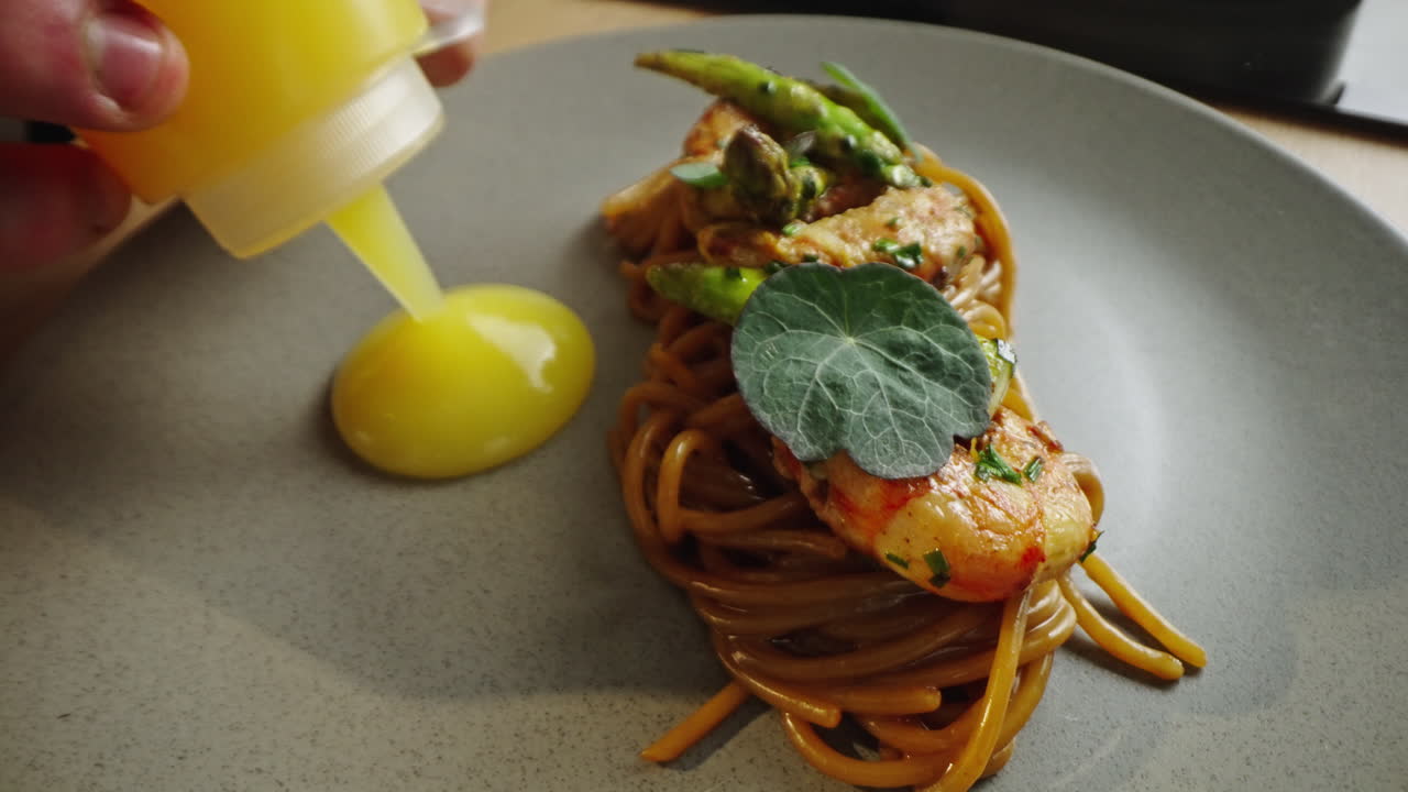Spaghetti with shrimp and asparagus being drizzled with yellow sauce