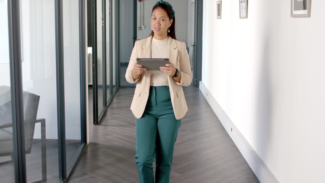 Walking in office hallway, woman holding tablet and smiling confidently