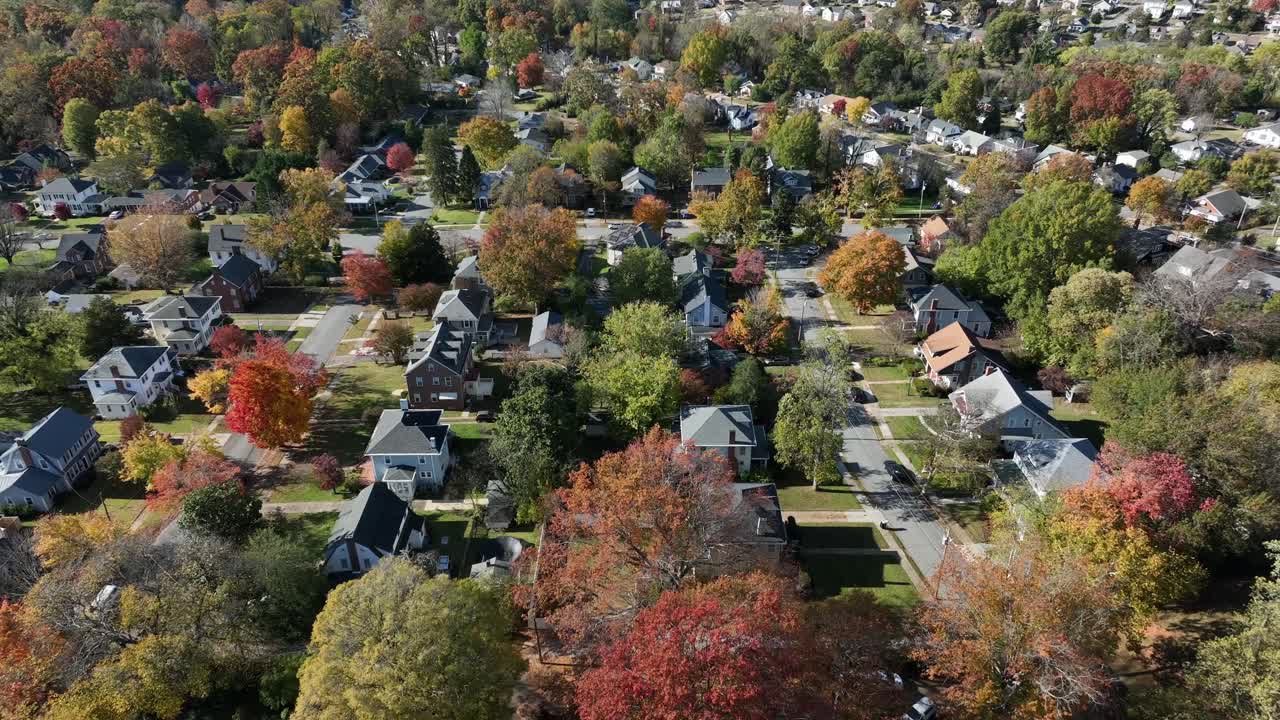 Aerial drone view gliding over a quiet American suburban neighborhood with colorful autumn trees, residential streets, and single-family homes captured in bright midday light