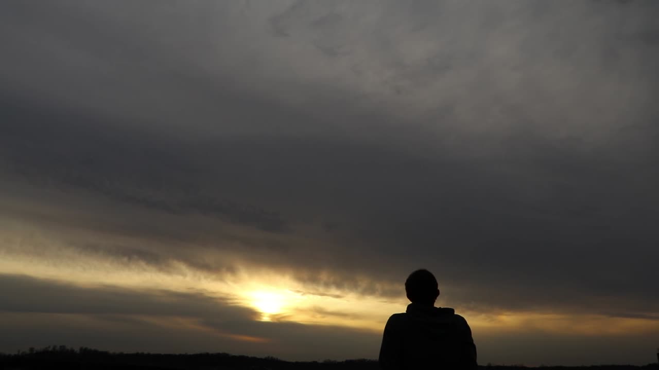 Young adult man gazes at vast sunset contemplating life. Self-exploration concept