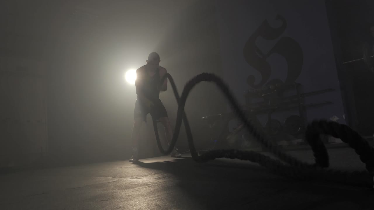 Boxer training with battle ropes in a smoky, atmospheric gym setting.