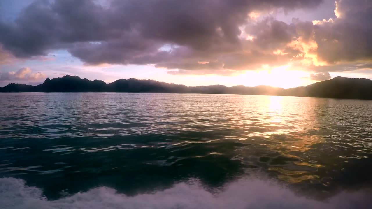 Bright Orange Sunset View of the Sea from a Boat, with Mountains and Dark Clouds.