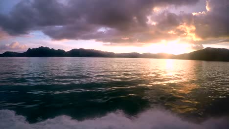 bright orange sunset view of the sea from a boat, with mountains and dark clouds.