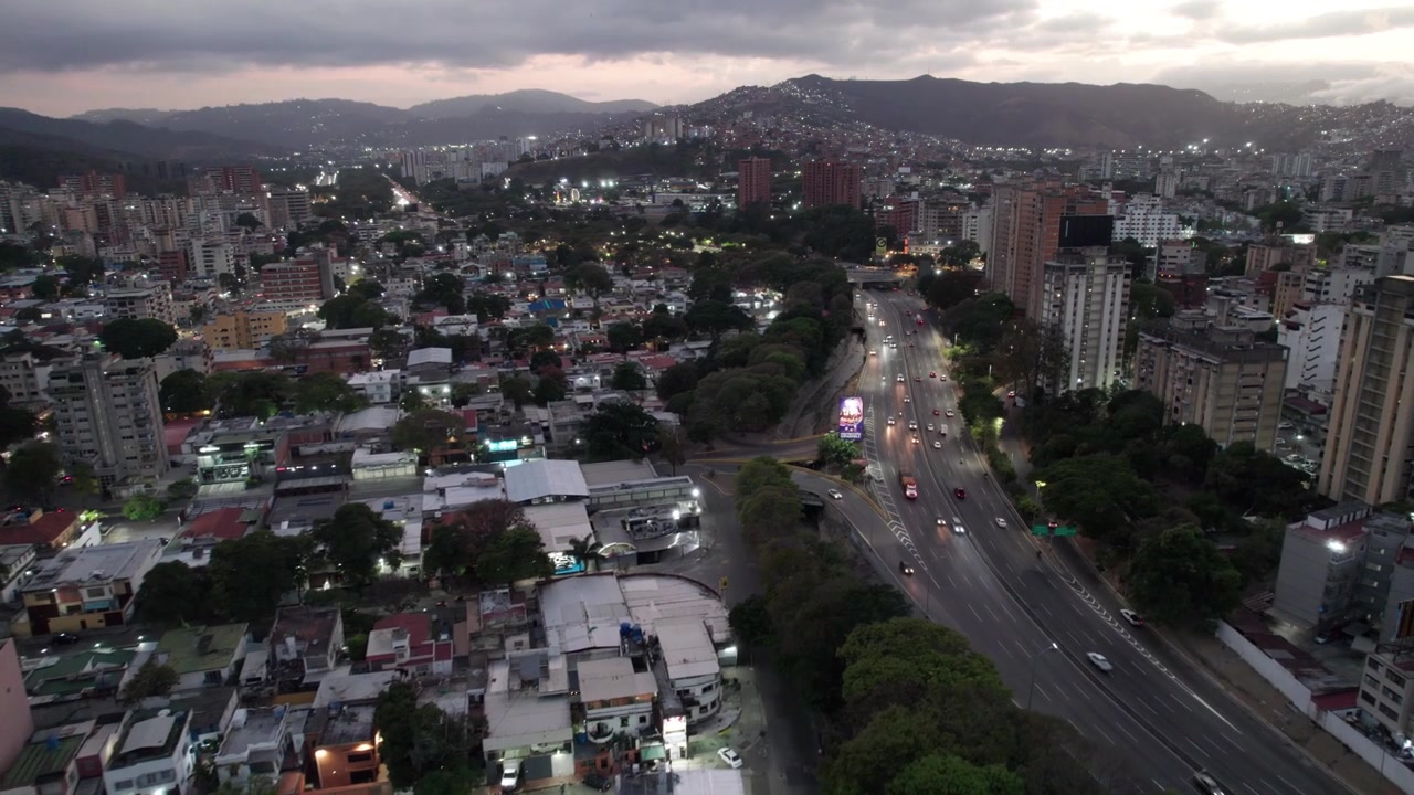 Vista panoramica dall'alto di auto in transito lungo un'autostrada urbana accanto a una zona residenziale al tramonto a Caracas
