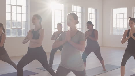 yoga class of young pregnant women practicing prayer pose enjoying healthy lifestyle group fitness workout in exercise studio at sunrise