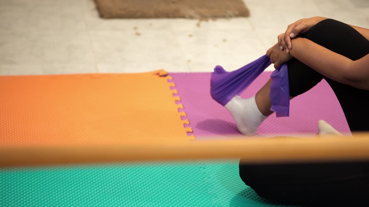 Person lying on mat using purple elastic band to stretch foot during therapy session
