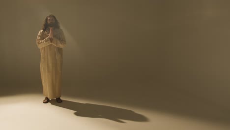 retrato de estudio de longitud completa de un hombre vestido con túnicas y sandalias con cabello largo y barba que representa la figura de jesucristo orando 1