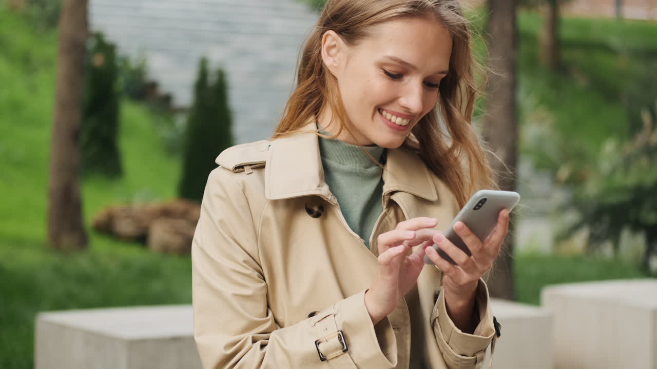 Happy Caucasian female student using smartphone outdoors.