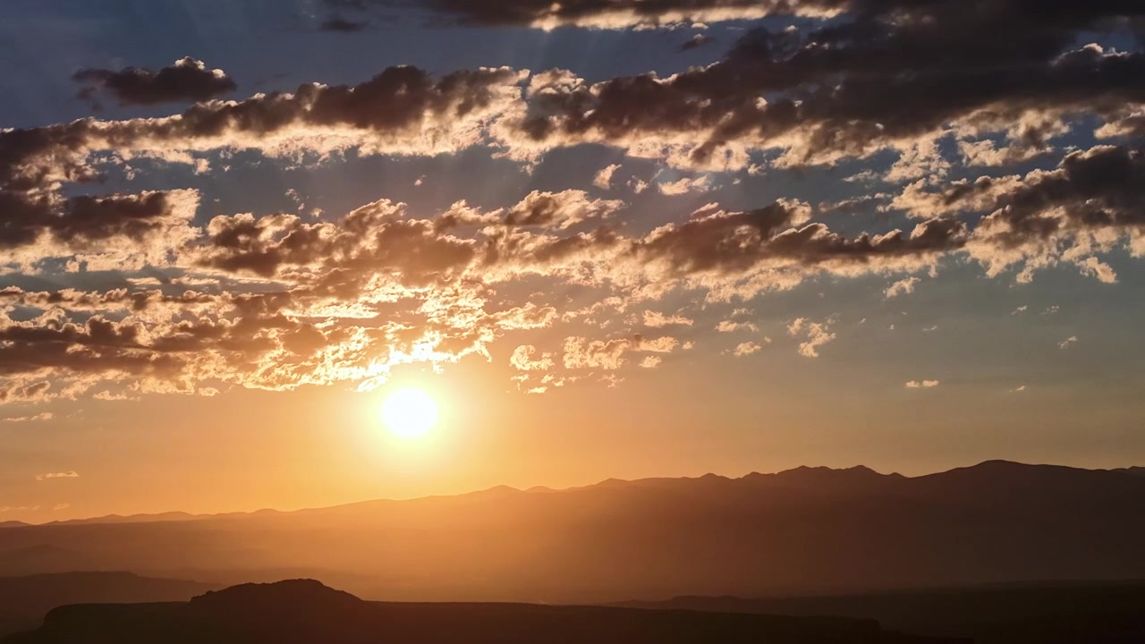 Timelapse de drone 4K UHD de um nascer do sol dourado brilhante. O sol resplandecente ascende por trás de uma crista montanhosa escura do Sudoeste, iluminando uma camada texturizada de nuvens matinais em um céu laranja vibrante.