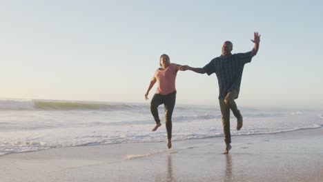 Lächelndes-älteres-Afroamerikanisches-Paar-Hält-Händchen-Und-Läuft-Am-Sonnigen-Strand