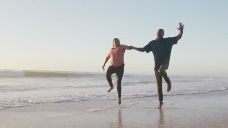 una pareja afroamericana de alto nivel sonriendo tomados de la mano y corriendo en una playa soleada