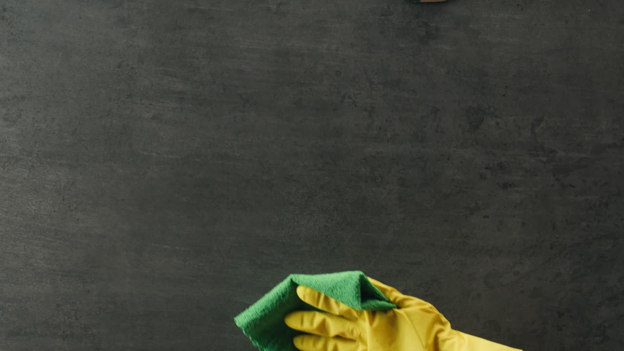 Hand in Yellow Glove Wiping Dark Surface with Green Cloth