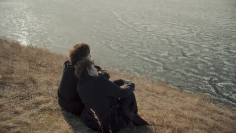 Romantic Couple Sitting Together by Frozen Lake and Enjoying View