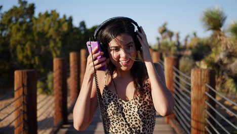 an attractive young hispanic woman walking and listening to music on her headphones with a smartphone while laughing and smiling slow motion