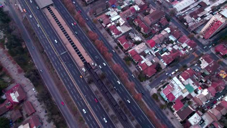 aerial top down dolly in of metro car riding between traffic in highway, low houses neighborhood on the sides, santiago, chile