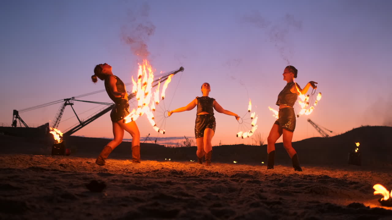 Professional artists show a fire show at a summer festival on the sand in slow motion. Fourth person acrobats from circus work with fire at night on the beach