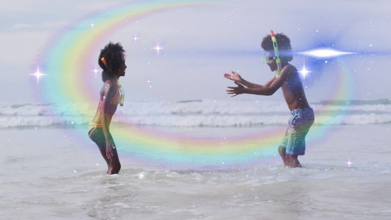 Children playing in ocean waves with rainbow and sparkles animation overlay