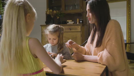 mother and her two little daughters playing chess at home 2