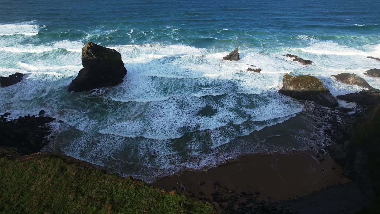Ripresa in picchiata con drone aereo sopra le Bedruthan Steps e le onde dell'oceano lungo la spiaggia in Cornovaglia