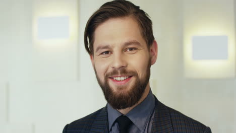 close-up view young caucasian bearded businessman in formal clothes looking at the camera and smiling in a meeting room