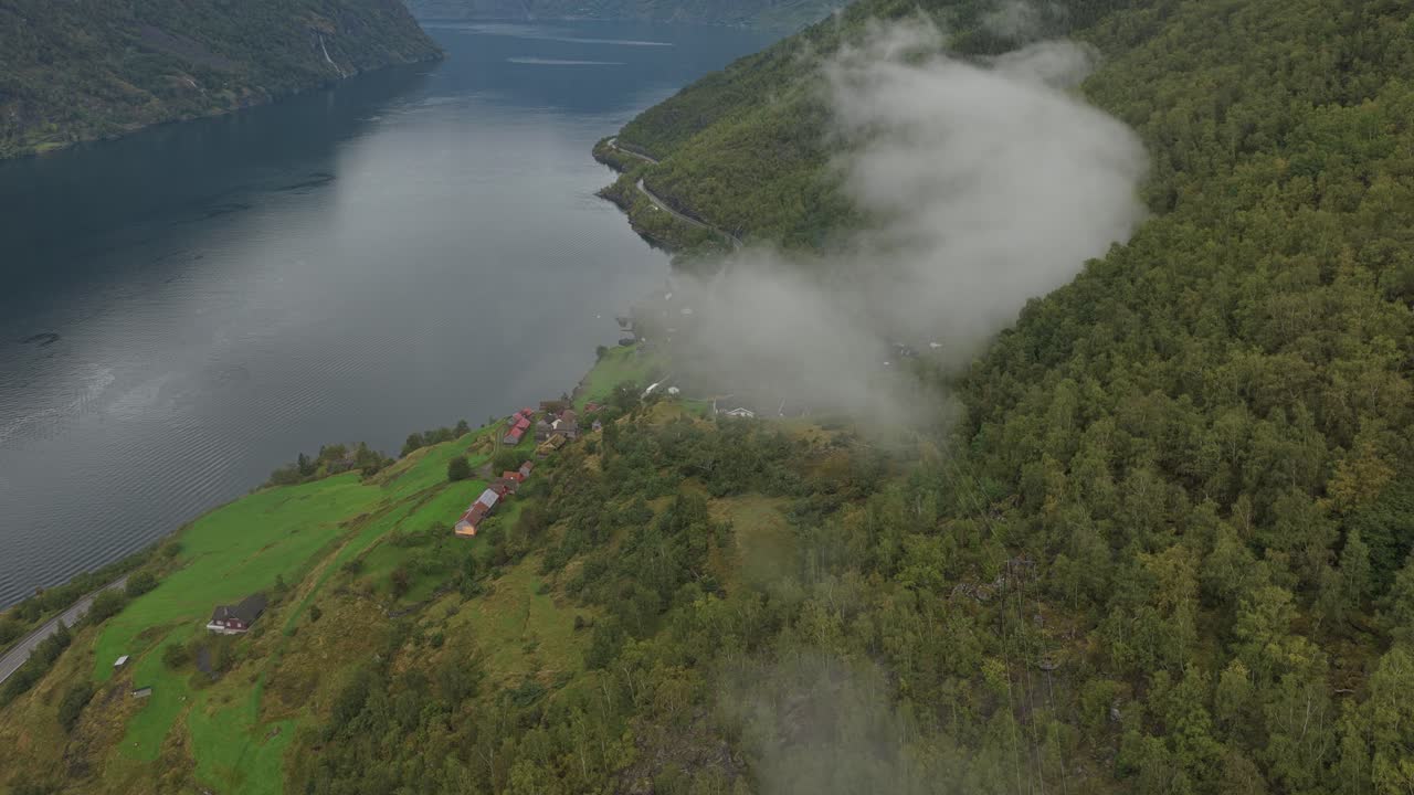 Droneudsigt over Otternes bygdetun ved fjordkanten under mørke skyer i Vestnorge