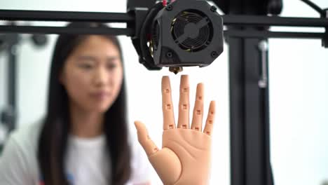 a young researcher observes a 3d printing process featuring a realistic robotic hand, showcasing the intersection of technology and innovation in robotics