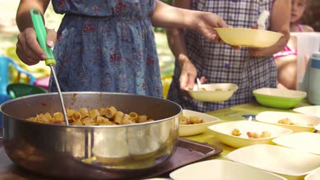 young happy kids preparing eating lunch pasta in summer camp outside on sunny day in park serving food from pot pan slow motion