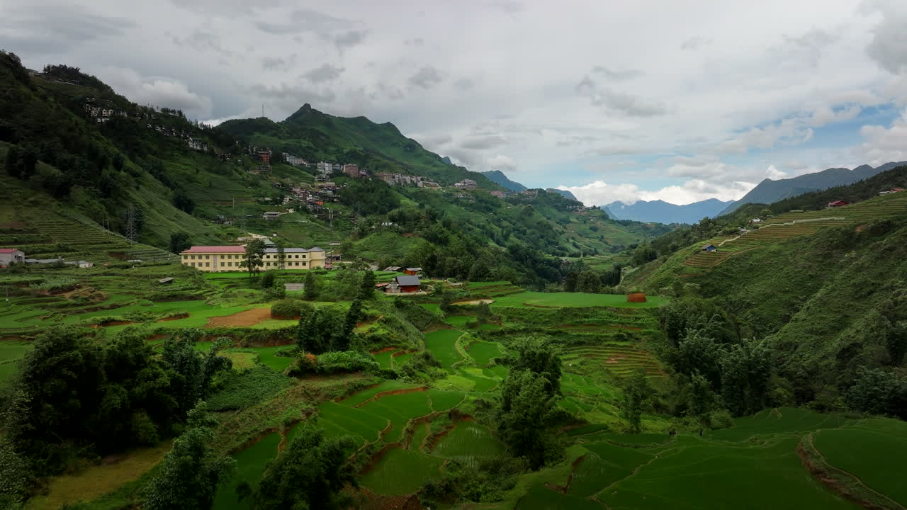 Drone establishing dolly over Sapa Valley terraced agricultural landscape with large buildings and farm houses along hillside