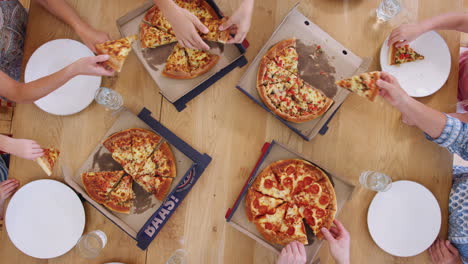 una foto aérea de una familia de varias generaciones sentadas alrededor de una mesa comiendo pizza juntos