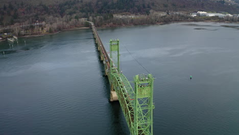 aerial view of a long green bridge spanning across a wide river with forested hills in the background